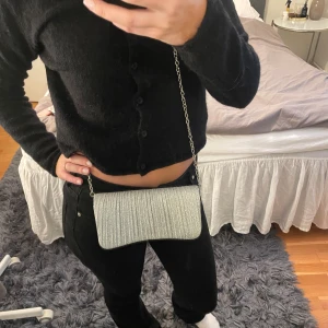 Glittrig silverfärgad väska - Snygg och glittrig väska i silver med en elegant kedja som axelrem. Perfekt för festliga tillfällen när du vill ha något litet och stilrent. Väskan har en enkel stängning och är tillräckligt rymlig för dina viktigaste saker. Den är i nyskick och redo att användas för en kväll ute!