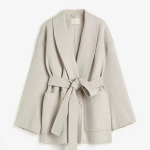 Ull Kappa - En snygg & mysig kappa med bälte i midjan och fickor på sidorna. Kappan är i en gråbeige färg och har en lös passform och otroligt mjukt tyg. Perfekt höstkappa / höstjacka.  Kappan är helt ny har endast testat.   Nypris 1999 kr. Slutsåld på hemsida. 