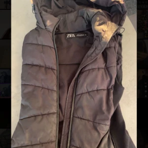 Svart pufferjacka från Zara - Säljer en svart pufferjacka från Zara i storlek M. Jackan har en dragkedja framtill och en mysig huva. Perfekt för kyliga dagar när du vill hålla dig varm och bekväm. Passar både till vardags och lite mer avslappnade tillfällen.
