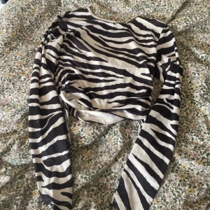 Zebramönstrad långärmad topp - Säljer en supercool zebramönstrad topp med långa ärmar. Den har en snygg snörning på sidan som ger en unik touch. Perfekt för att sticka ut på festen eller bara för en vardag med stil!