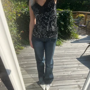 Svart mönstrad topp från KappAhl - Säljer en snygg svart topp från KappAhl i storlek 44/46. Den är ärmlös och har ett vitt, detaljerat mönster som ger en elegant touch. Perfekt för både vardag och fest! Mycket stretchig. Axelbredd: 35 cm och längd: 60 cm.