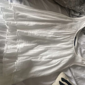 Vit klänning från Gina Tricot - Säljer en superfin vit klänning från Gina Tricot. Den är ärmlös och har en luftig och lätt design, perfekt för sommardagar. Klänningen har volanger som ger den en romantisk touch. Materialet känns mjukt och bekvämt mot huden.
