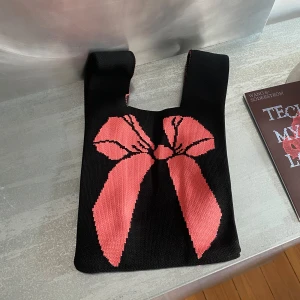 Stickad väska med rosettmotiv - Coquette stickad väska i svart med rosettmotiv på.