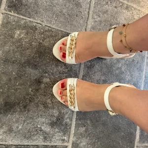 Vita sandaler med guldkedja - Säljer ett par snygga vita sandaler från Romerro i storlek 36. De har en elegant guldkedja som detalj och en bekväm klack. ! De är i väldigt bra skick och redo för dig att passa på o köpa 💖🌸🌸