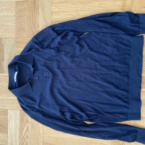 Mörkblå pikétröja från Zara - Säljer en stilren mörkblå pikétröja från Zara. Tröjan har långa ärmar och en klassisk krage med knappar. Perfekt för både vardag och lite mer uppklädda tillfällen. Passar bra till jeans eller chinos!