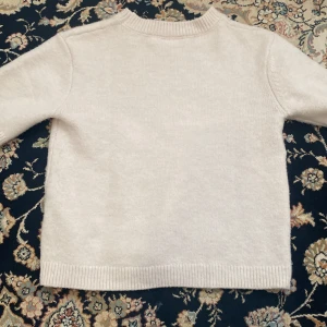 Beige stickad tröja från Kappahl - Mysig beige stickad t-shirt från Kappahl. Perfekt för kyliga dagar med sin mjuka och bekväma passform. Tröjan har korta ärmar och ribbade kanter vid hals, ärmslut och nederkant. En klassisk och stilren design som passar till det mesta! Säljer eftersom den kommer aldrig till användning 