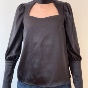 Svart blus med puffärmar - Snygg svart blus med puffiga långa ärmar och en unik fyrkantig halsringning. Perfekt för både vardag och festliga tillfällen. Materialet är mjukt och liknar siden