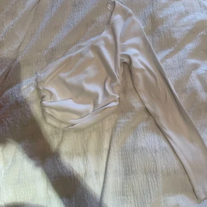 Vit långärmad topp från Zara - Säljer en elegant vit långärmad topp från Zara. Den är gjord i ett mjukt och glansigt material som ger en lyxig känsla. Perfekt för både vardag och festliga tillfällen. Toppen har en stilren design med en åtsittande passform.