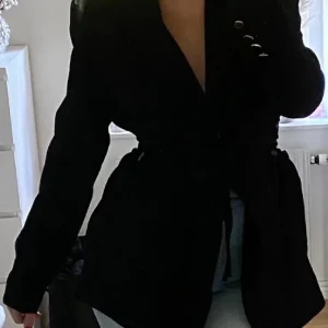 Svart blazer med snörning  - Säljer en stilren svart kavaj från Dilvin Woman i storlek 36. Kavajen har en klassisk design med knappar på ärmarna och ett bälte i midjan för en snygg passform. Perfekt för både vardag och fest!. Är i nyskick! Lånad bild!