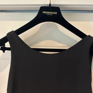 Svart klänning från Pronovias - Säljer en klänning från Pronovias. Den har en vacker, glittrig detaljering på kjolen som ger en lyxig känsla. Klänningen är ärmlös och har en lång flytande design som passar perfekt för festliga tillfällen. Materialet känns exklusivt. nköpt på milagr