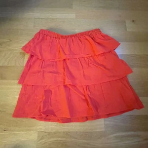 Röd volangkjol från H&M Divided - Säljer en superfin röd volangkjol från H&M Divided. Kjolen har flera lager av volanger som ger en härlig och lekfull look. Perfekt för sommardagar eller en festlig kväll! Den är i storlek XXS och har en elastisk midja för extra komfort.