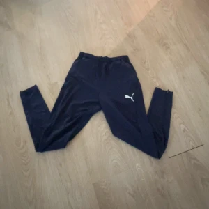 Svarta träningsbyxor från Puma - Säljer ett par svarta träningsbyxor från Puma i storlek S. Byxorna har en enkel och stilren design med Pumas logga på ena benet. Perfekta för träning eller en avslappnad dag hemma. De är tillverkade i ett bekvämt material som ger bra rörelsefrihet.