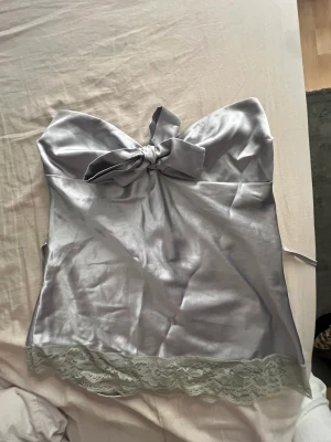 Söt topp  - Super fin fest topp som man kan knyta där bak så att den blir tajt i midjan. Som ny!  Det står ingen storlek men skulle säga S-M!  Bandeau topp i silver med rosett.