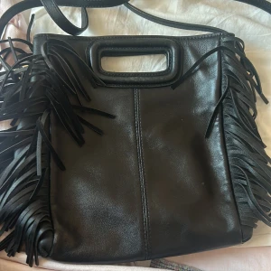 Svart axelväska med fransar från Maje - Säljer en supercool svart axelväska från Maje. Den är gjord i skinn och har snygga fransar på sidorna.  Väskan har ett praktiskt handtag och en justerbar axelrem. Perfekt för både vardag och fest! Nypris 3 295 kr!! Äkta såklart!
