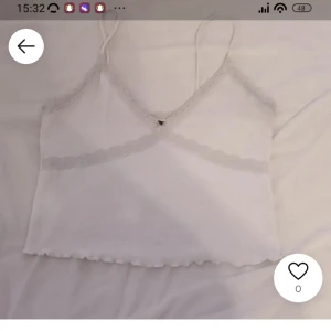 Vit spetskantad linnetopp - Säljer en söt vit linnetopp med smala axelband och spetsdetaljer längs halsringningen. Toppen är croppad och har en lätt vågig kant nertill. Perfekt för sommardagar eller som ett lager under en kofta. 