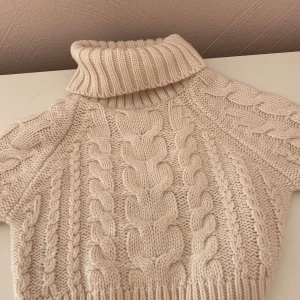 Beige stickad polotröja från Gina Tricot - Säljer en supermysig beige stickad polotröja från Gina Tricot. Den har ett snyggt flätmönster och en hög polokrage som håller dig varm under kyliga dagar. Perfekt för höst och vinter! Tröjan är i storlek XXS och är i nyskick. Perfekt för att mysa till det i stil! 🍂✨