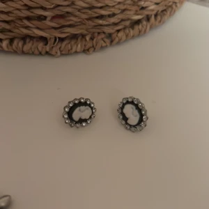 Svarta och vita örhängen med pärldetaljer - Eleganta örhängen med svart och vit design, omgivna av små pärlor. Perfekta för att ge en klassisk touch till din stil.