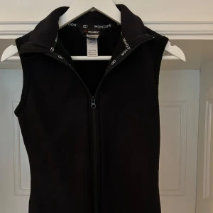 Svart fleeceväst från Mondor - Svart väst i det varma materialet polarfleece, mycket bra kvalitet. Märket är populärt inom konståkning men fungerar väl även till vardags. Stl XS. Se storleksguide i bilden. Nypris +1000 kr.