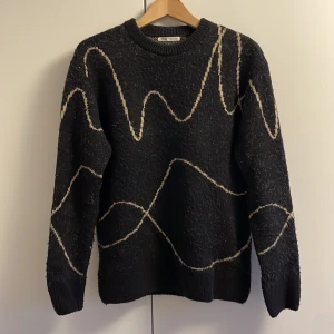 Svart stickad tröja från Zara - Säljer en svart stickad tröja från Zara med ett unikt vågigt mönster i beige. Tröjan har långa ärmar och en rund halsringning. Riktigt mjukt tjockt tyg! Skriv direkt vid minsta frågetecken!