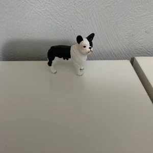 Schleich hund - En liten svartvit hundfigur i plast, perfekt för samlare eller som dekoration. Figuren har en realistisk design med detaljerade drag och står stadigt på sina fyra ben.
