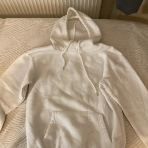 Vit hoodie med ficka - Säljer en klassisk vit hoodie med stor ficka framtill och justerbar huva. Perfekt för en avslappnad stil. Den är mjuk och bekväm, idealisk för kyligare dagar.