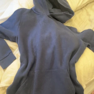Mörkblå hoodie - Säljer en mörkblå hoodie med klassisk design. Den har en stor ficka framtill och en bekväm huva. Perfekt för en avslappnad stil.