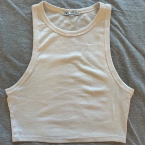 Vit ribbad linnetopp från Zara - Säljer en stilren vit ribbad linnetopp från Zara. Toppen är ärmlös och croppad, perfekt för varma dagar. Den har en klassisk rund halsringning och är gjord i ett mjukt och stretchigt material. Finns i Uppsala för upphämtning eller skickas.