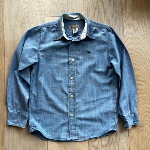 Blå skjorta från L.O.G.G. - Snygg blå långärmad skjorta från L.O.G.G. med broderad detalj på bröstet. Skjortan har knappar framtill och en klassisk krage. Perfekt för en stilren look.