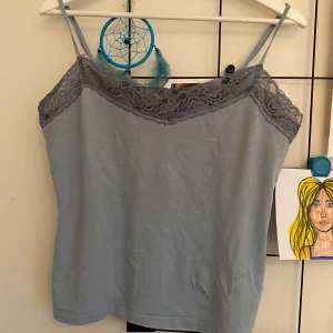 Ljusblå linnetopp med spetsdetaljer - Snygg ljusblå linnetopp med smala axelband och vacker spetsdetalj längs överkanten. Axelbanden är justerbara.