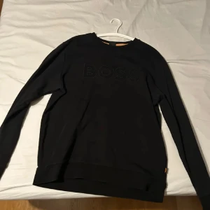 Svart tröja från Boss - Säljer en stilren svart tröja från Boss med diskret logga på bröstet. Tröjan har långa ärmar och en klassisk passform. Perfekt för en avslappnad men ändå snygg look.