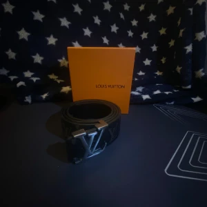 Svart bälte från Louis Vuitton - Snyggt svart bälte från Louis Vuitton med ett stilrent LV-spänne i silver. Bältet har en diskret mönstring och är tillverkat i skinn. Perfekt för att ge en lyxig touch till din outfit.Kan sänka pris vid snabb affär
