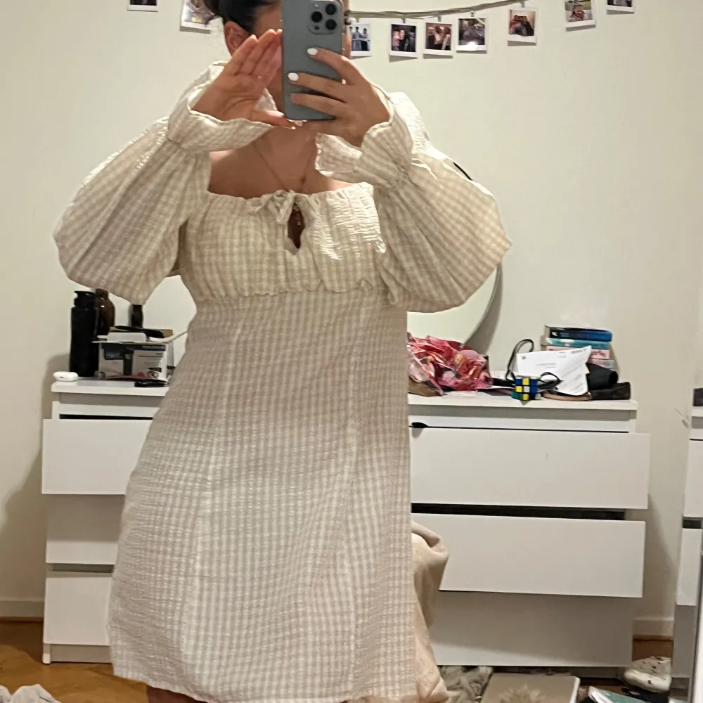 Charmig beige rutig klänning med långa puffärmar och en söt knytning framtill. Perfekt för en avslappnad och stilren look. Den har en kort längd och använt 2 gånger.. Mekot.
