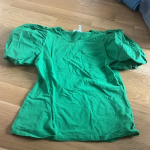 Grön topp med puffärmar - Säljer en grön topp med puffiga kortärmar. Den har en rund halsringning och är tillverkad i ett mjukt material. Perfekt för en färgglad look!