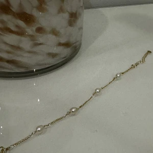 Guldarmband med pärlor - Elegant guldarmband med fyra vita pärlor. Armbandet har en justerbar kedja och en enkel karbinhake för säker stängning. Perfekt för att ge en sofistikerad touch till din stil.