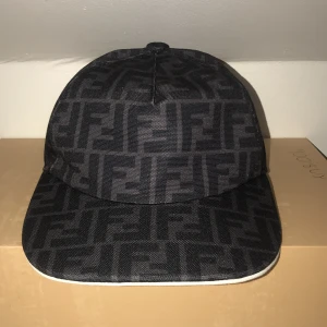 Svart keps från Fendi - Snygg svart keps från Fendi med ett diskret mönster i grått. Kepsen har en justerbar rem baktill för perfekt passform. Perfekt accessoar för en stilren look. PRISET KAN DISKUTERAS!!    Vill bli Ahmed den för jag inte använder den längre ingen förpackning!
