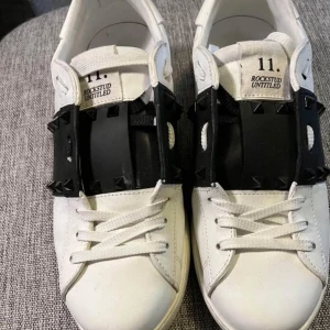 Valentino skor  - Snygga vita Valentino Rockstud Untitled sneakers med svarta detaljer och snörning. Skorna har de ikoniska rockstuds på sidan och en stilren design som passar perfekt för en trendig look.