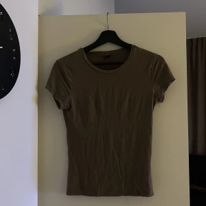 Brun t-shirt från Gina Tricot - Säljer en brun t-shirt från Gina Tricot i storlek S. T-shirten har en enkel design med korta ärmar och rund hals. Perfekt för en avslappnad stil.