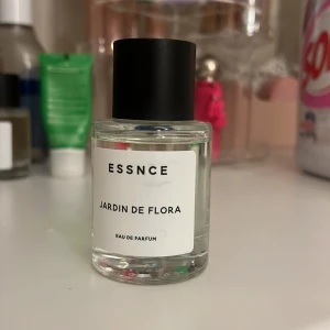 Jardin de Flora Eau de Parfum från Essnce - Elegant Eau de Parfum med en fräsch och blommig doft. Flaskan är stilren och genomskinlig med en svart kork och vit etikett. Perfekt för den som älskar en naturlig och sofistikerad doft.