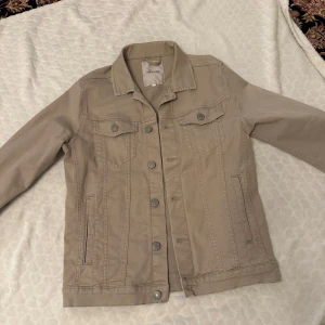 Beige jeansjacka från Jack & Jones - Säljer en stilren beige jeansjacka från Jack & Jones. Jackan har knappar framtill och två bröstfickor med knappstängning. Perfekt för en avslappnad look.