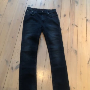 Svarta jeans från Nudie Jeans - Snygga svarta jeans från Nudie Jeans med klassisk femficksdesign och knappgylf. Jeansen har en rak passform och är tillverkade i högkvalitativt denim. Perfekta för en stilren look.