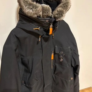 Svart Peak Performance parkajacka med pälsdetaljer - Exklusiv rejäl svart parkajacka från Peak Performance med huva och pälsdetaljer. Jackan har flera praktiska fickor och dragkedja med knappar. Perfekt för kalla dagar. Mycket gott skick, som ny. Hipe.