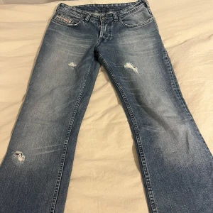 Lågmidjade jeans från diesel - Supersnygga, lågmidjade straight/flare jeans från Diesel. Snygga hål på benen. Står storlek 31 men passar ändå bra på mig som brukar ha 28 i waist. De är klippta och uppsydda så de är lagom på någon som är 160 och under. Midjemått mätt rakt över är 40 cm och grenhöjden, från midjan till grenen är 22 cm. I mycket bra skick! ☺️