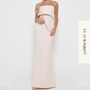 Ljusrosa axelbandslös långklänning - Elegant ljusrosa axelbandslös långklänning med en stilren design. Klänningen har en slits baktill och en vacker omlott-detalj vid bysten. Perfekt för balen. Helt oanvänd och säljer pga fel storlek