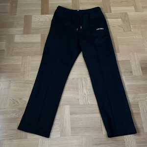 Svarta byxor från Les Deux - Snygga svarta byxor från Les Deux med en minimalistisk design. Byxorna har en elastisk midja med snörning för extra komfort. Perfekta för en stilren look. Skick: 10/10 nästan aldrig använda!