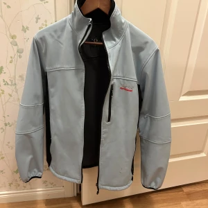 Ljusblå softshelljacka från Pesk Performance  - Säljer en ljusblå softshelljacka från Peak med svarta detaljer. Jackan har en dragkedja framtill och hög krage. Några små svarta streck längs ner men syns knappt. Går nog och ta bort. Köpt i Kina.