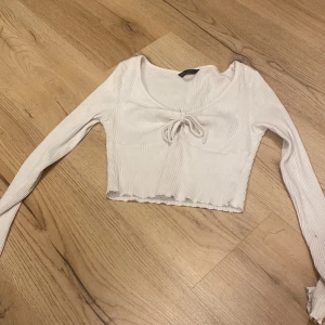 Vit ribbad croppad topp - Säljer en vit ribbad croppad topp med långärmad design och en söt knytning framtill. Perfekt för en stilren och trendig look.