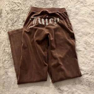 Bruna mjukisbyxor från Juicy Couture - Snygga bruna mjukisbyxor från Juicy Couture med glittrig text på baksidan. Byxorna har en bekväm passform och är perfekta för en avslappnad stil. Tillverkade i mjukt material för extra komfort.