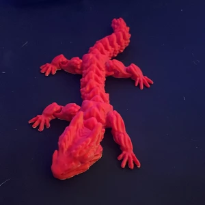 Rörlig drake  - En röd 3D-printad drake med detaljerade fjäll och fyra ben. Draken har en lång, böjd svans och en skulpterad huvudform. Perfekt som dekoration eller leksak.