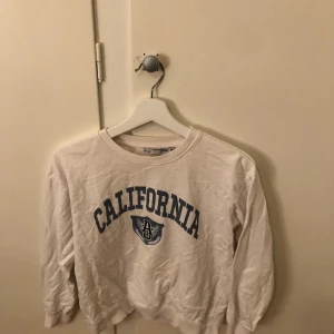 Vit sweatshirt med tryck från 157 - Säljer en vit sweatshirt från 157 med texten 'California' och ett tryck på framsidan. Tröjan har långa ärmar och en rund halsringning. Perfekt för en avslappnad stil.