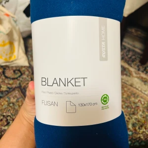 Blå filt från Rusta Home - Mysig blå filt från Rusta Home, modell Flisan, i storlek 130x170 cm. Tillverkad av 100% återvunnen polyester och certifierad enligt OEKO-TEX standard. Perfekt för att hålla sig varm under kyliga kvällar.